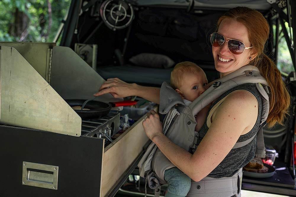 mom using baby camping gear carrier to entertain baby while cooking camping meal