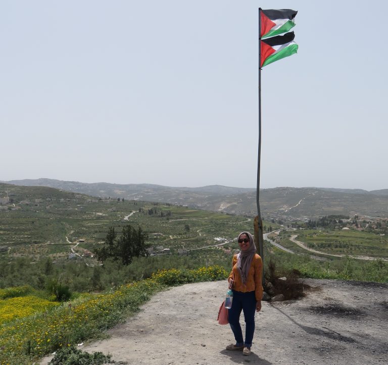 Haya poses with the Palestinian flag on a sunny day in Sebastia, a village on the outskirts of Nablus.