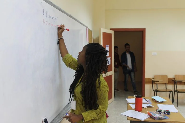 EFL Fellow Mecca writes on the board as students enter the classroom in the first week of EFL class.