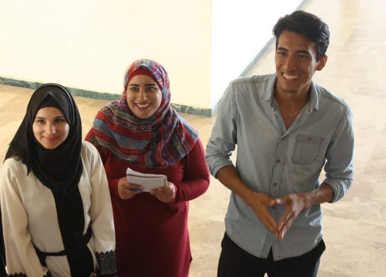 Two EFL students and their teacher enjoy listening to a speaking activity.