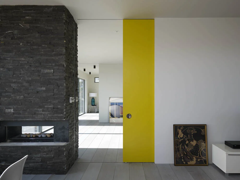 large two sided stone chimney with yellow pocket door in white contemporary home