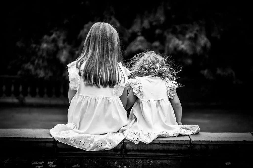 Artistic black and white photo from behind of two young sisters sitting together on a low wall at Belle Vue Park, Newport, taken by Emotion Picture Photography.