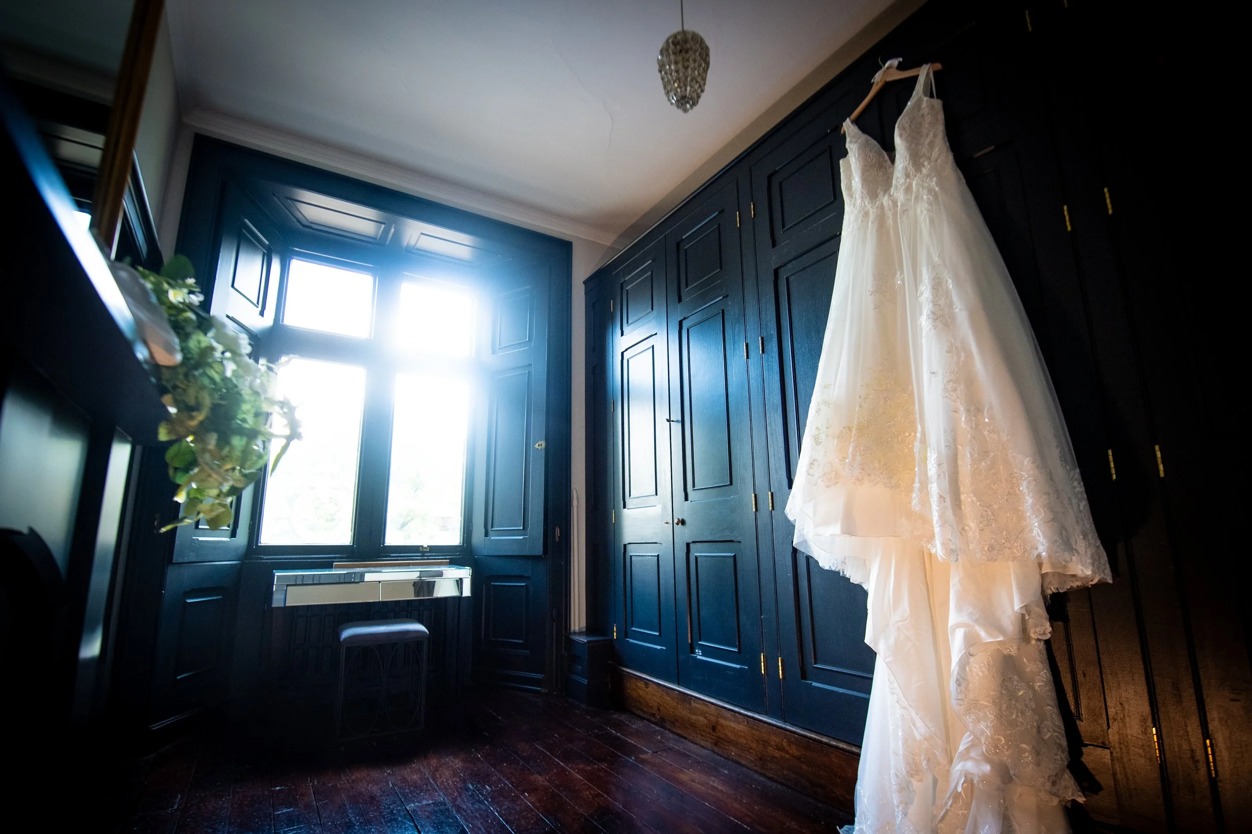 Lace wedding dress hanging in the dark wood paneled bridal suite at Cefn Tilla Court