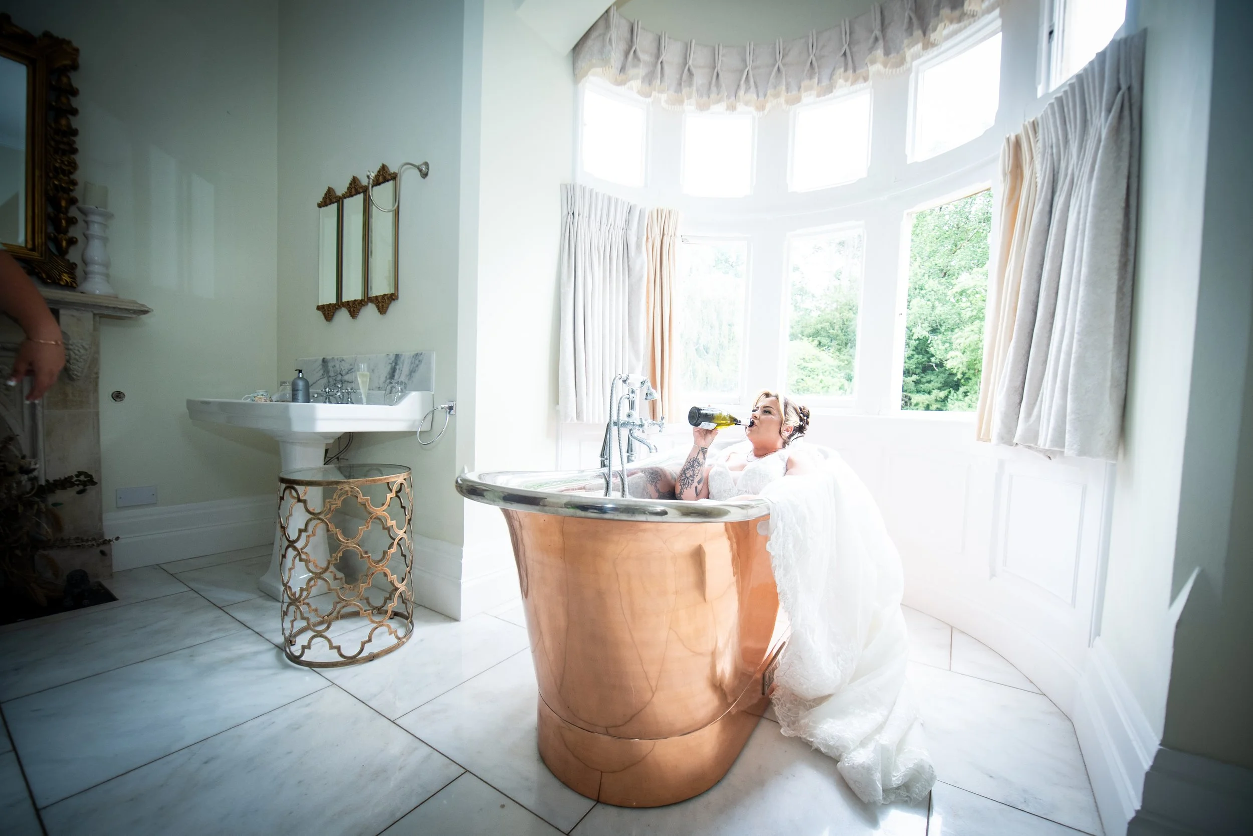  Bride enjoying a playful moment in a freestanding copper bathtub during wedding prep at Cefn Tilla Court