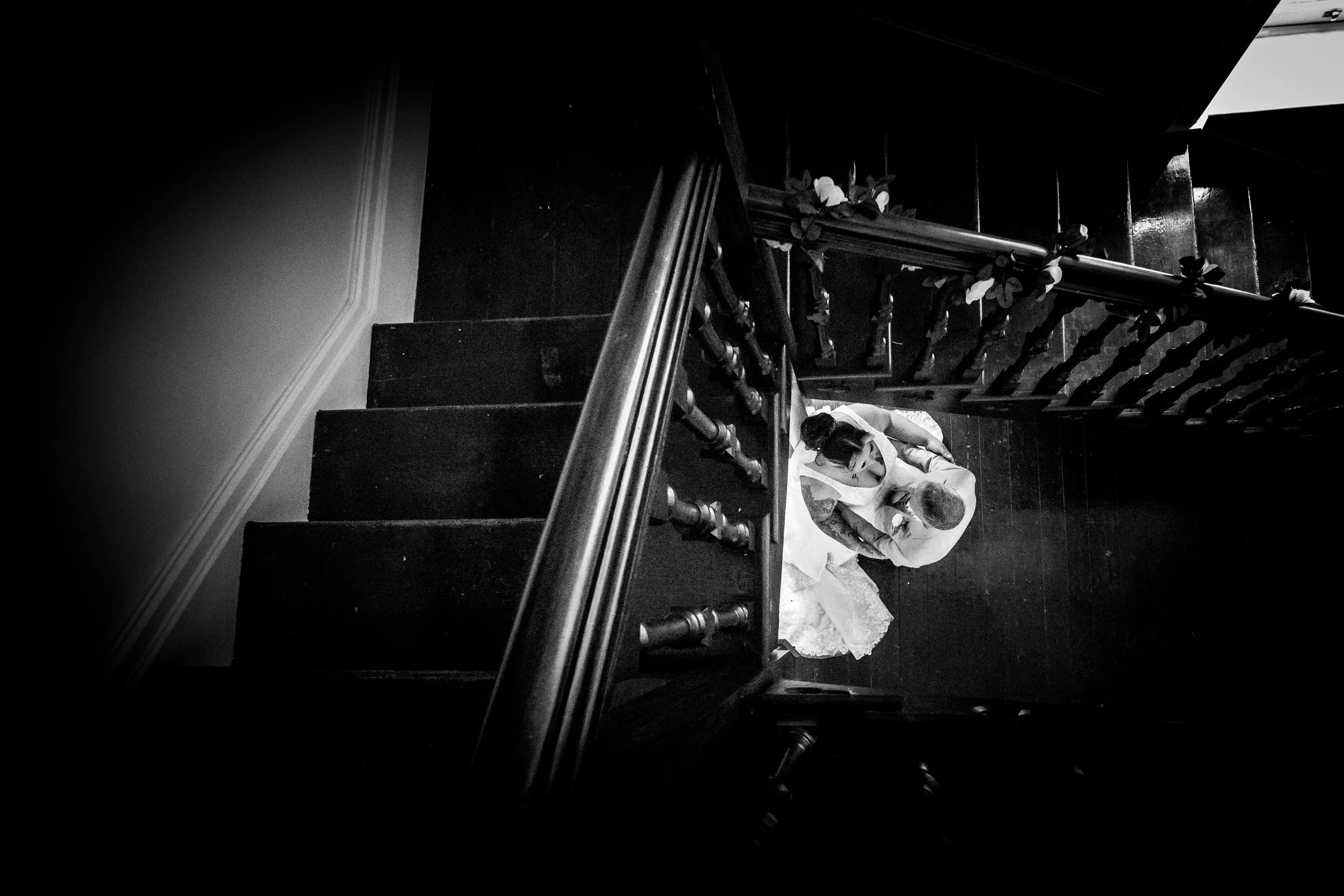 Atmospheric black and white photograph of a quiet moment on the historic dark wood staircase at Cefn Tilla Court