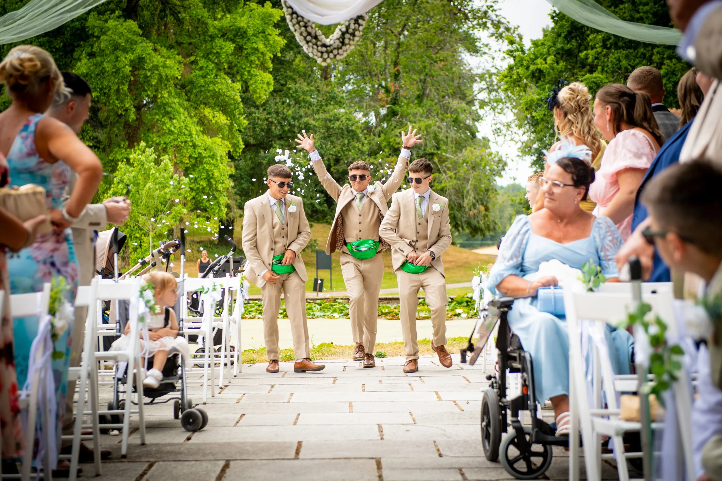  Groom and groomsmen walking down the outdoor aisle past happy guests at Cefn Tilla Court