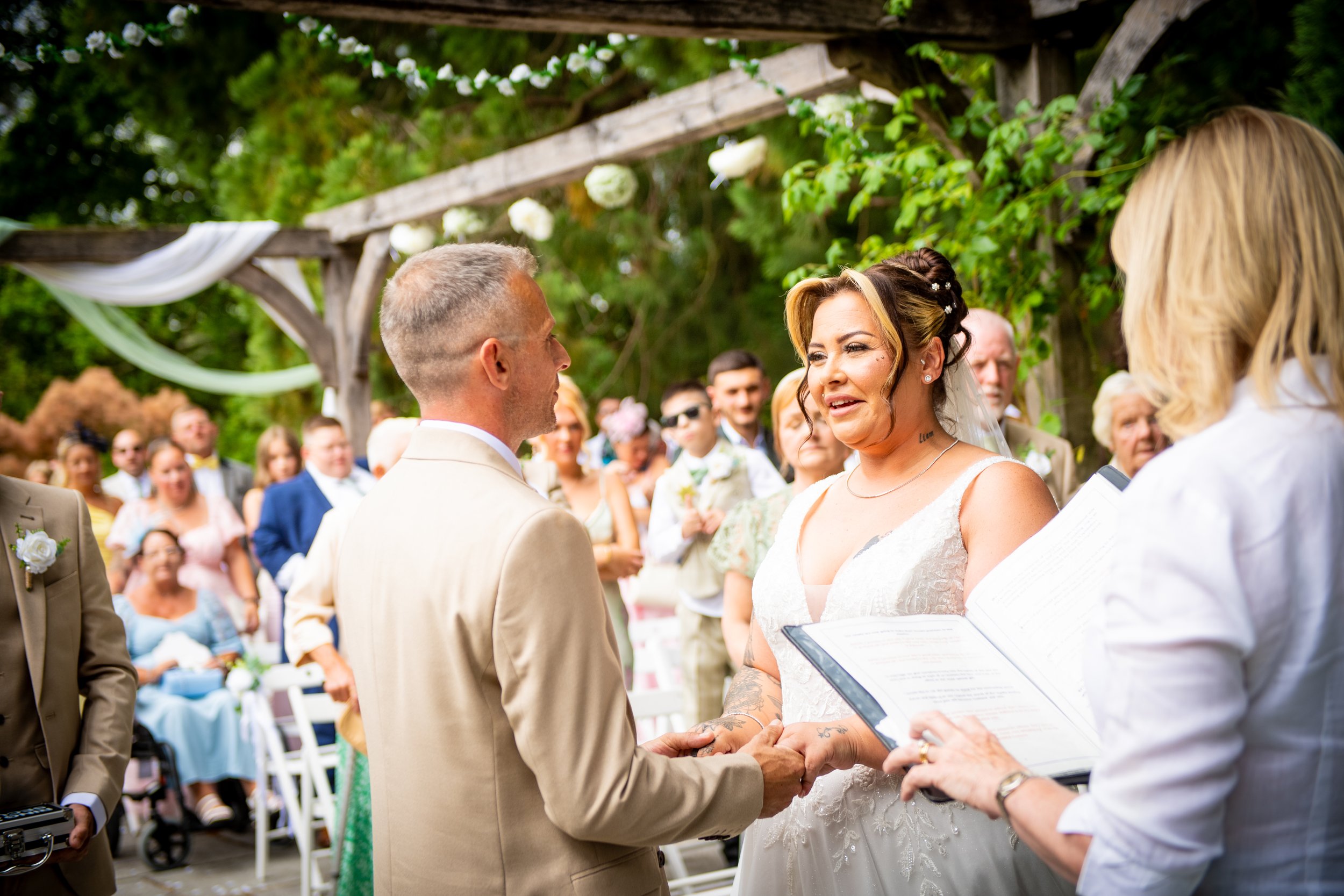 Couple exchanging vows under a wooden floral arbor during an outdoor ceremony in South Wales