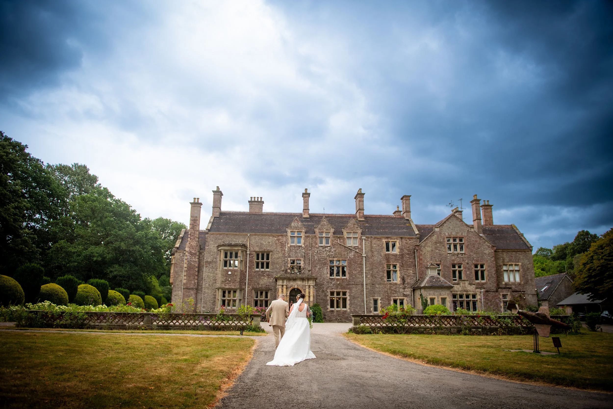 Bride and groom walking together in front of the historic stone manor house at Cefn Tilla Court