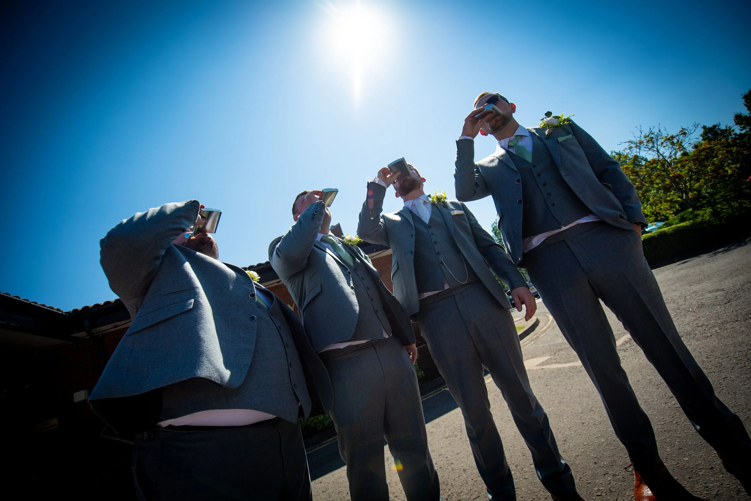 Groom and groomsmen drinking from hip flasks outside in the bright summer sunshine before a Parkway Hotel wedding