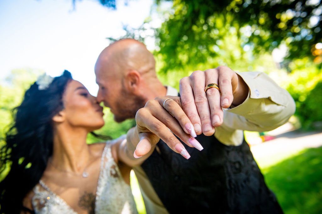 Close up of a newlywed couple showing off their new wedding rings while kissing in the background