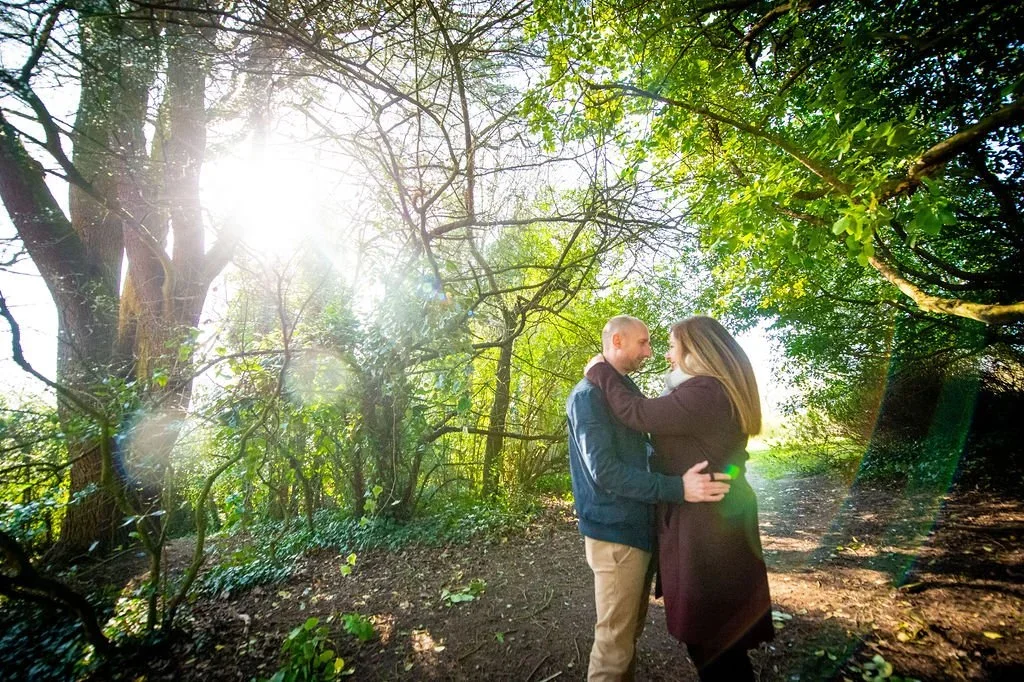 A couple embracing in a wooded forest under sunlight.