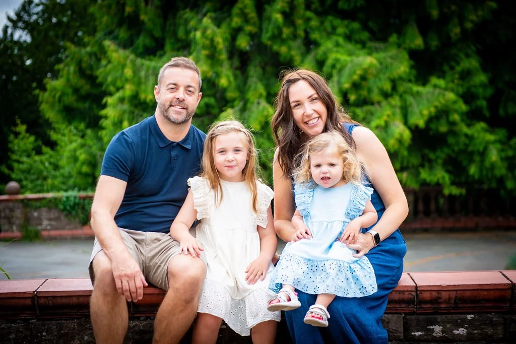 Happy family of four sitting together outdoors for a vibrant color portrait session at Belle Vue Park in Newport with Emotion Picture Photography.