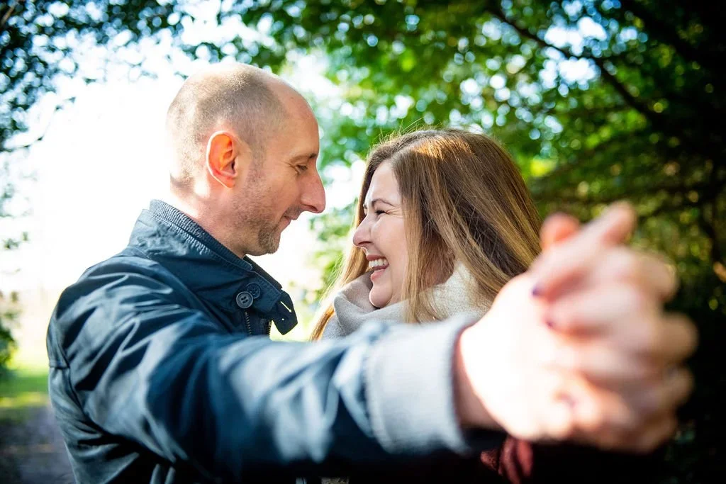 A couple dancing outdoors, smiling, with trees in the background.