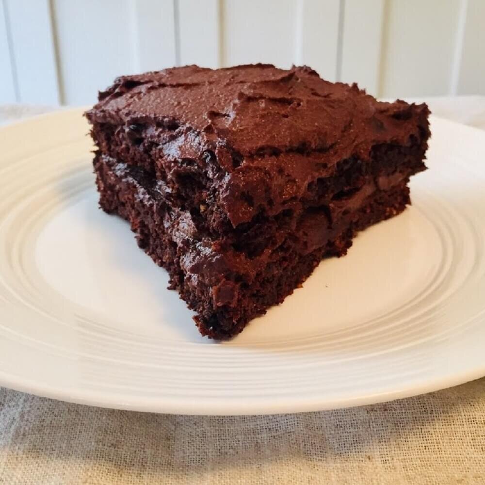 vegan gluten free chocolate cake slice on a white plate with a linen tablecloth underneath.