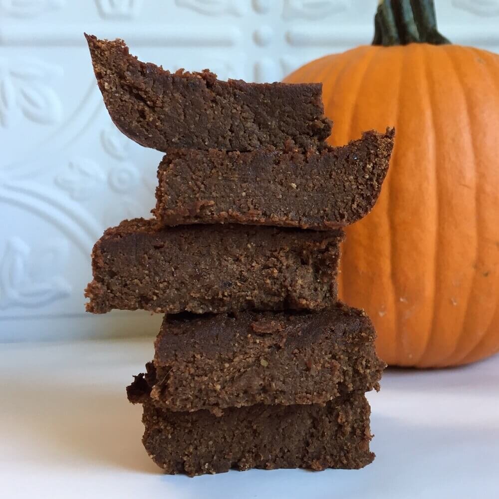 vegan pumpkin brownies stacked with a pumpkin in the background