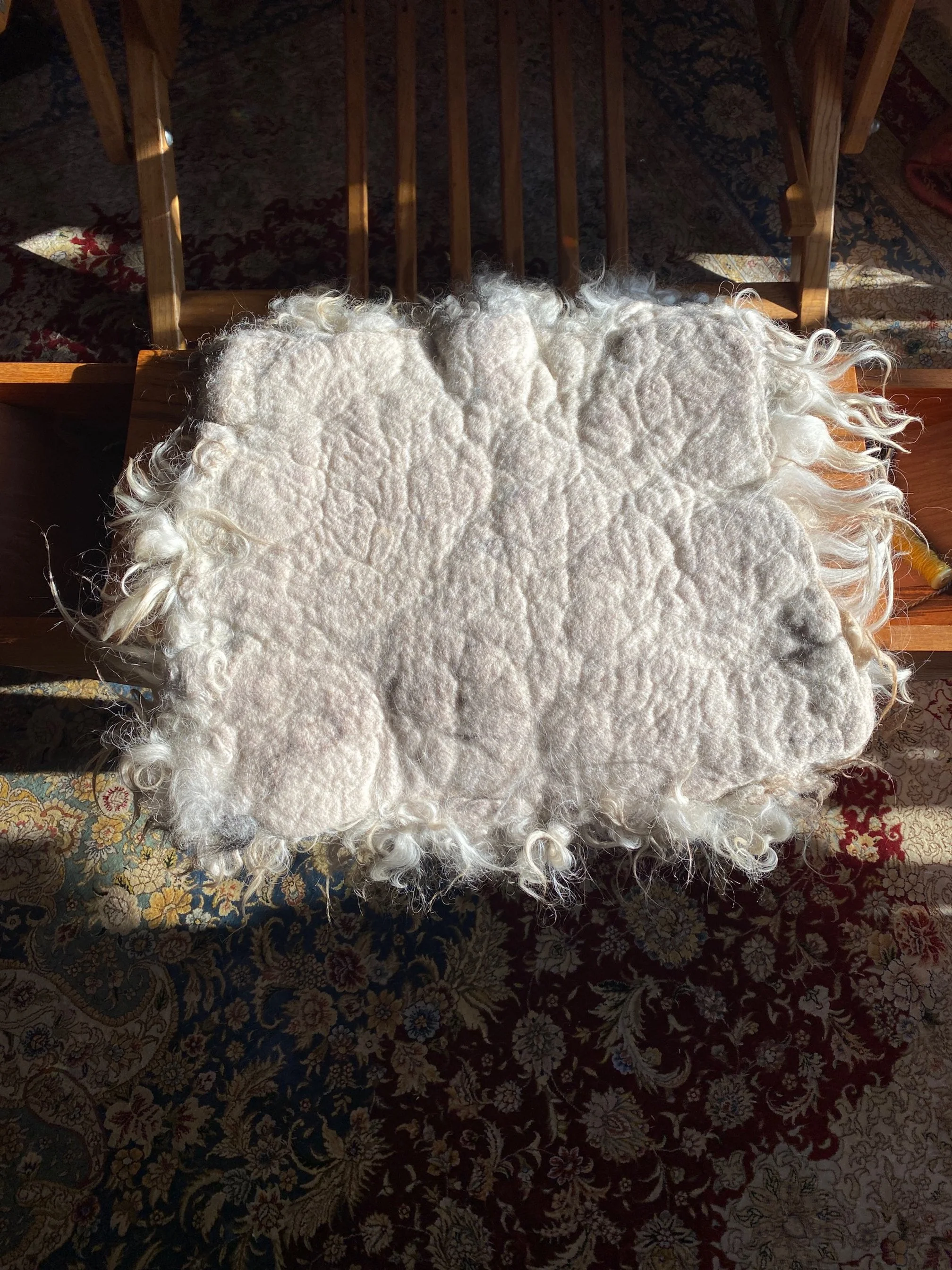 Backside of vegetarian sheepskin pad made of felted wool, shown on a chair seat.