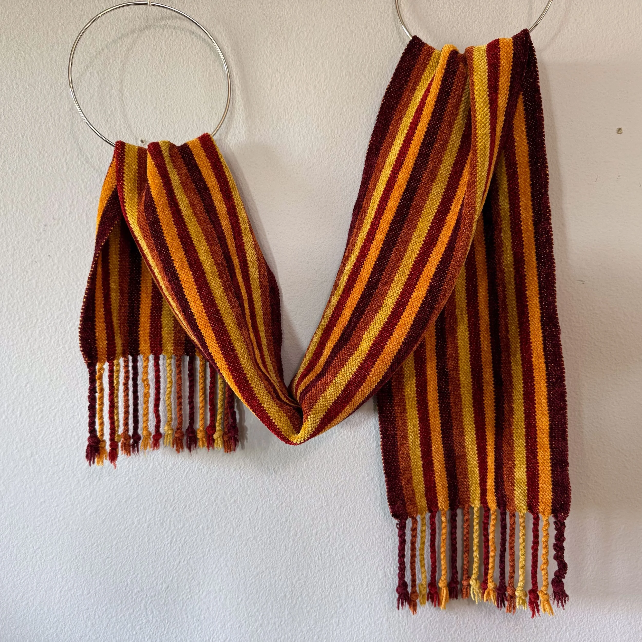 Chenille scarf  in fall colors draped from rings .