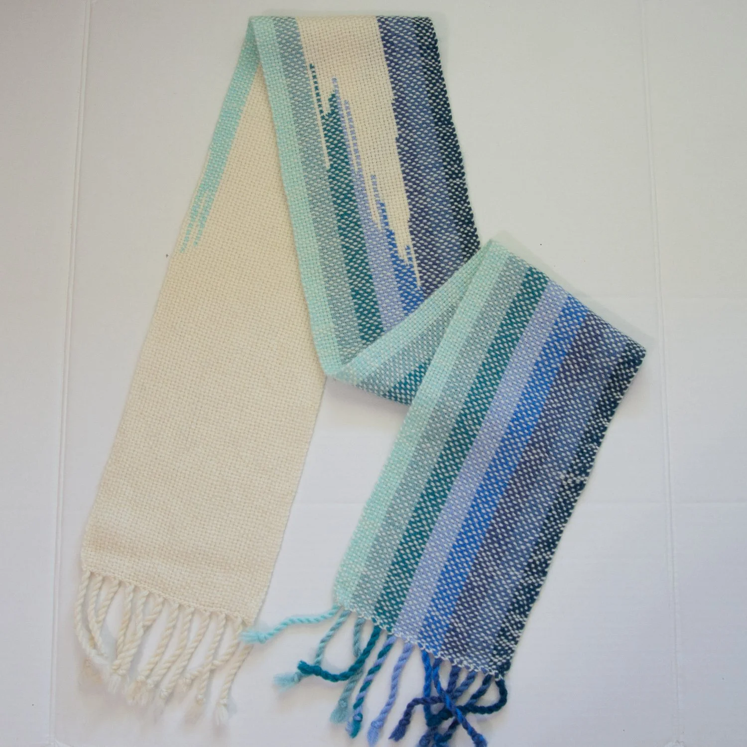 Handwoven scarf in white and several shades of blue, woven in clasped warp technique.