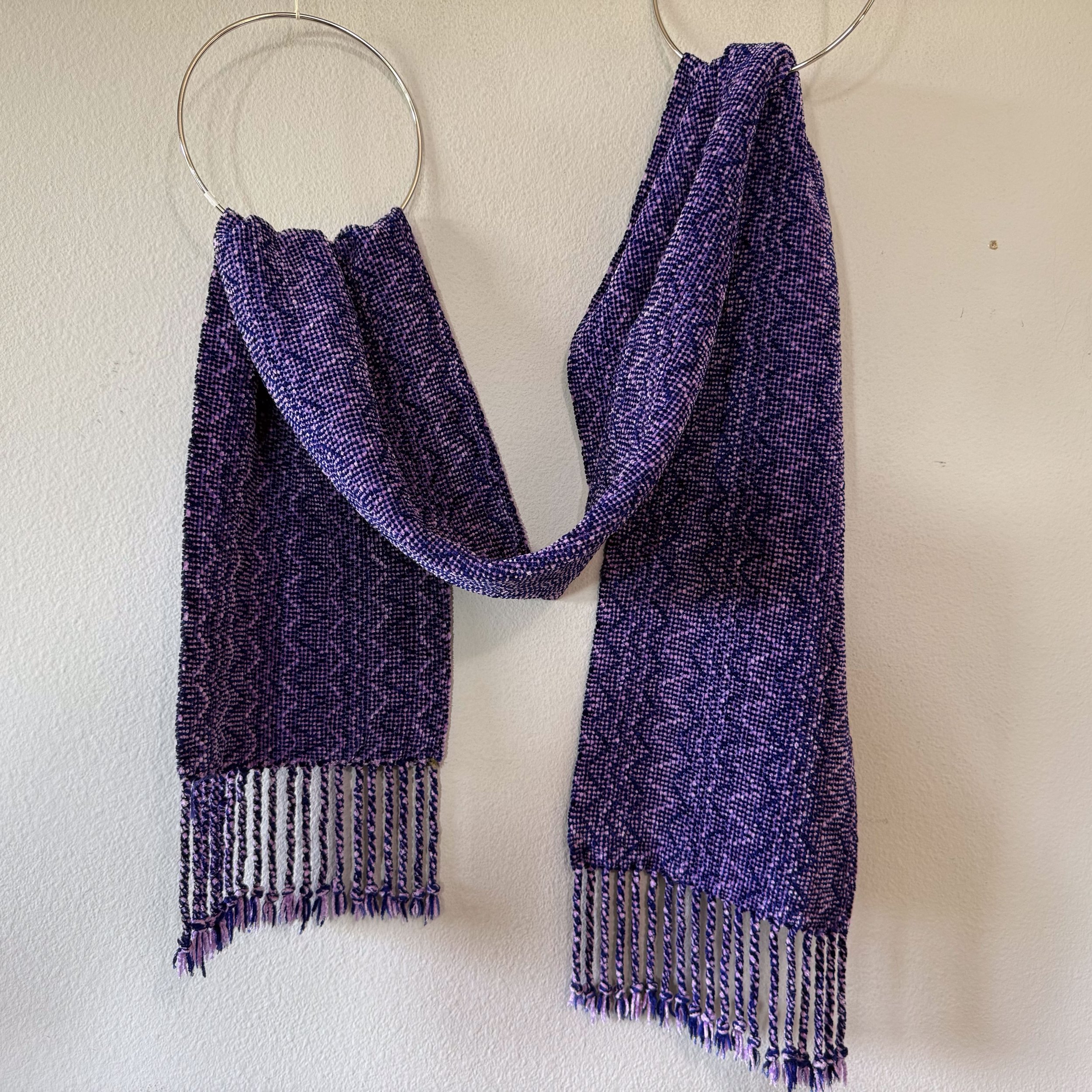 Purple rayon chenille scarf displayed in two rings on wall.
