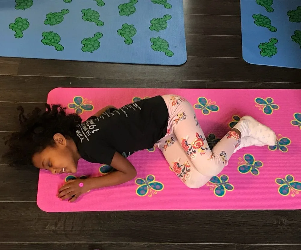 A young child in relaxation pose on a pink yoga mat.