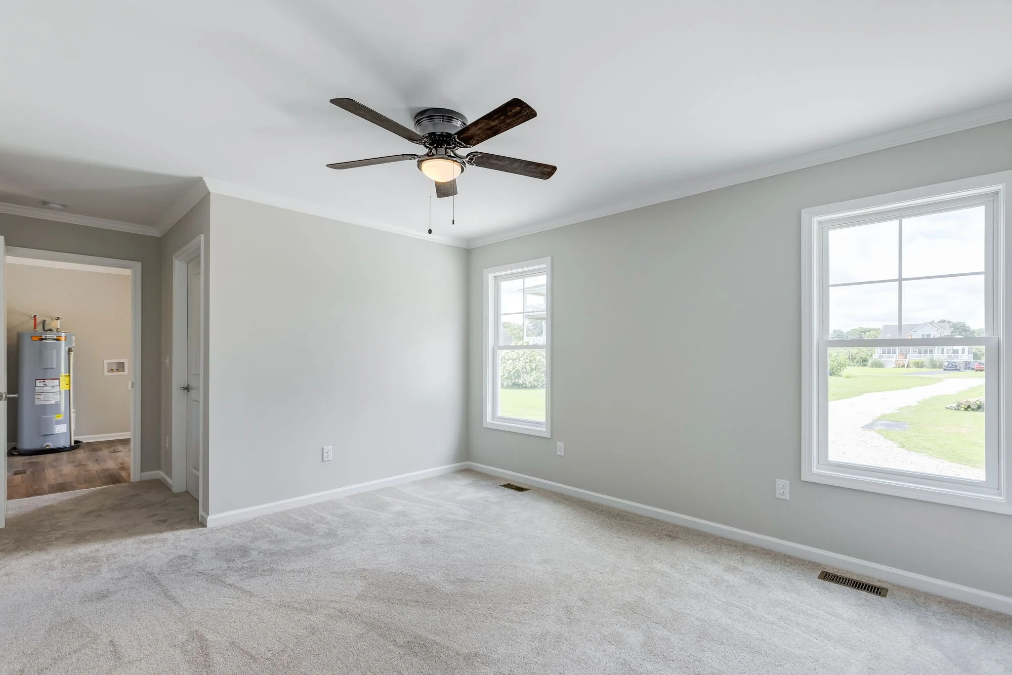 Empty living room with white walls, beige carpet, two windows, and a ceiling fan with light.