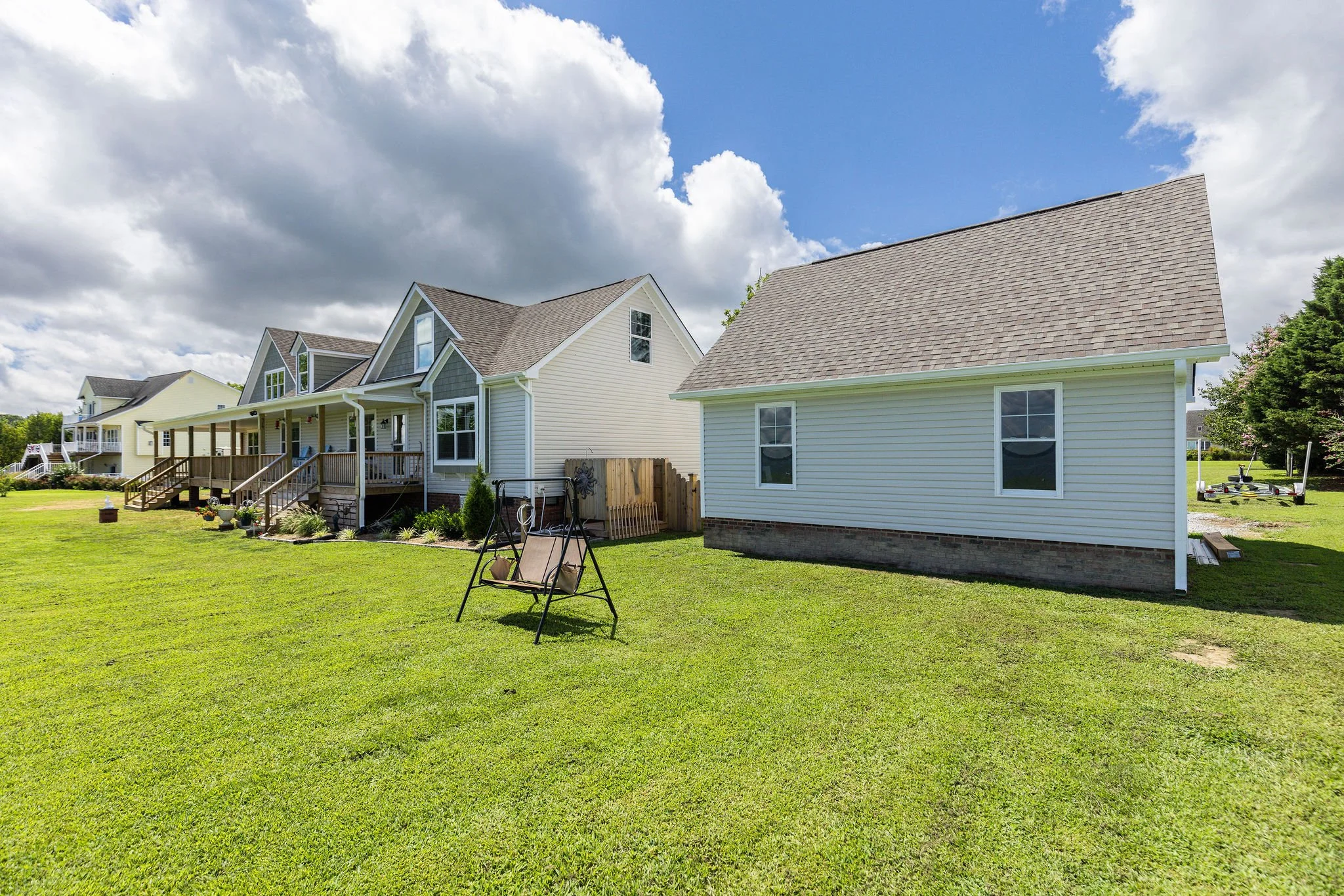 A backyard with green grass, a swing, and a row of houses with porches and decks under a partly cloudy sky.