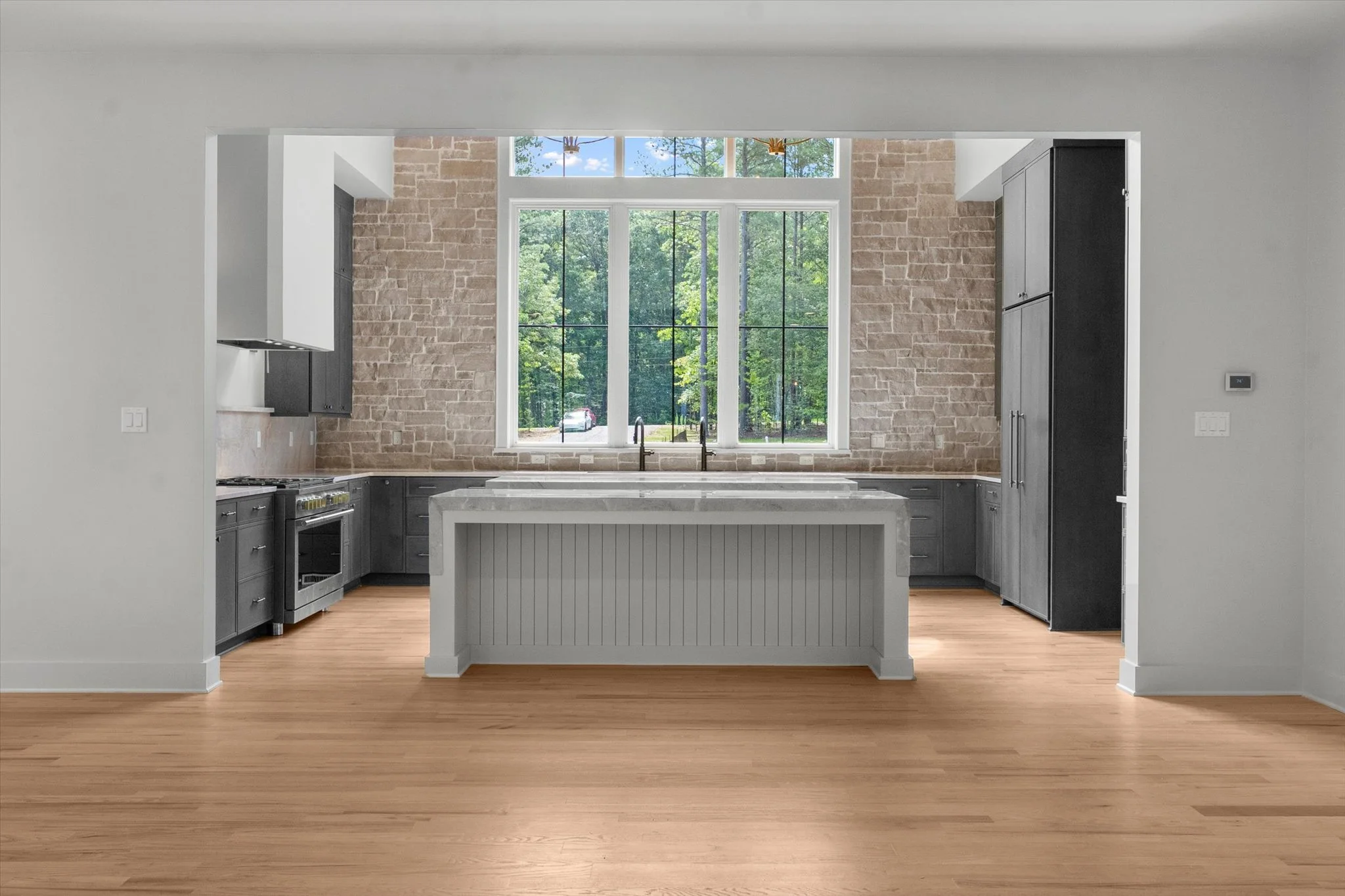 Modern kitchen with gray cabinets, a white island, brick accent wall, large window, and hardwood floors.