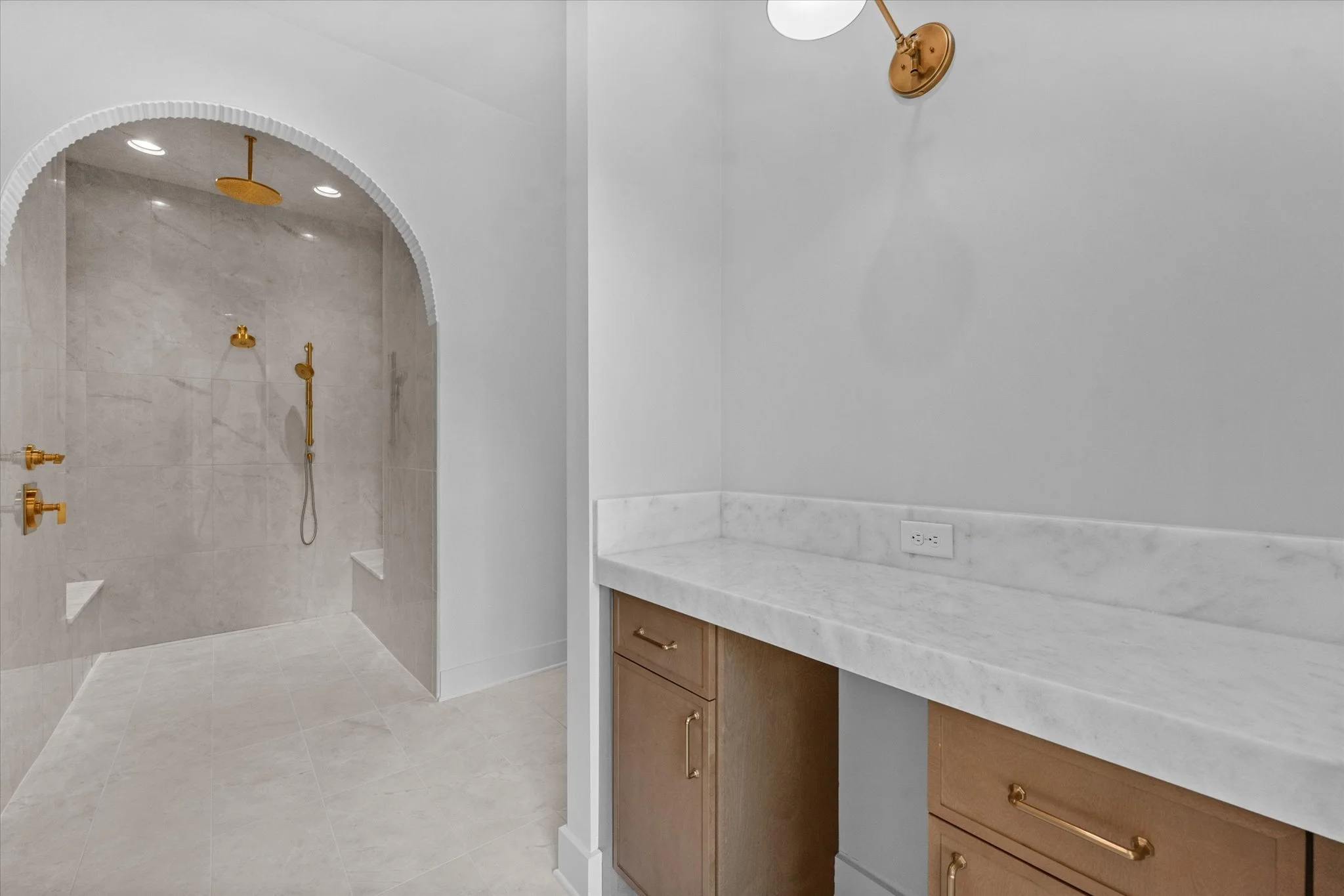 Modern bathroom with a marble countertop and a walk-in shower with gold fixtures.