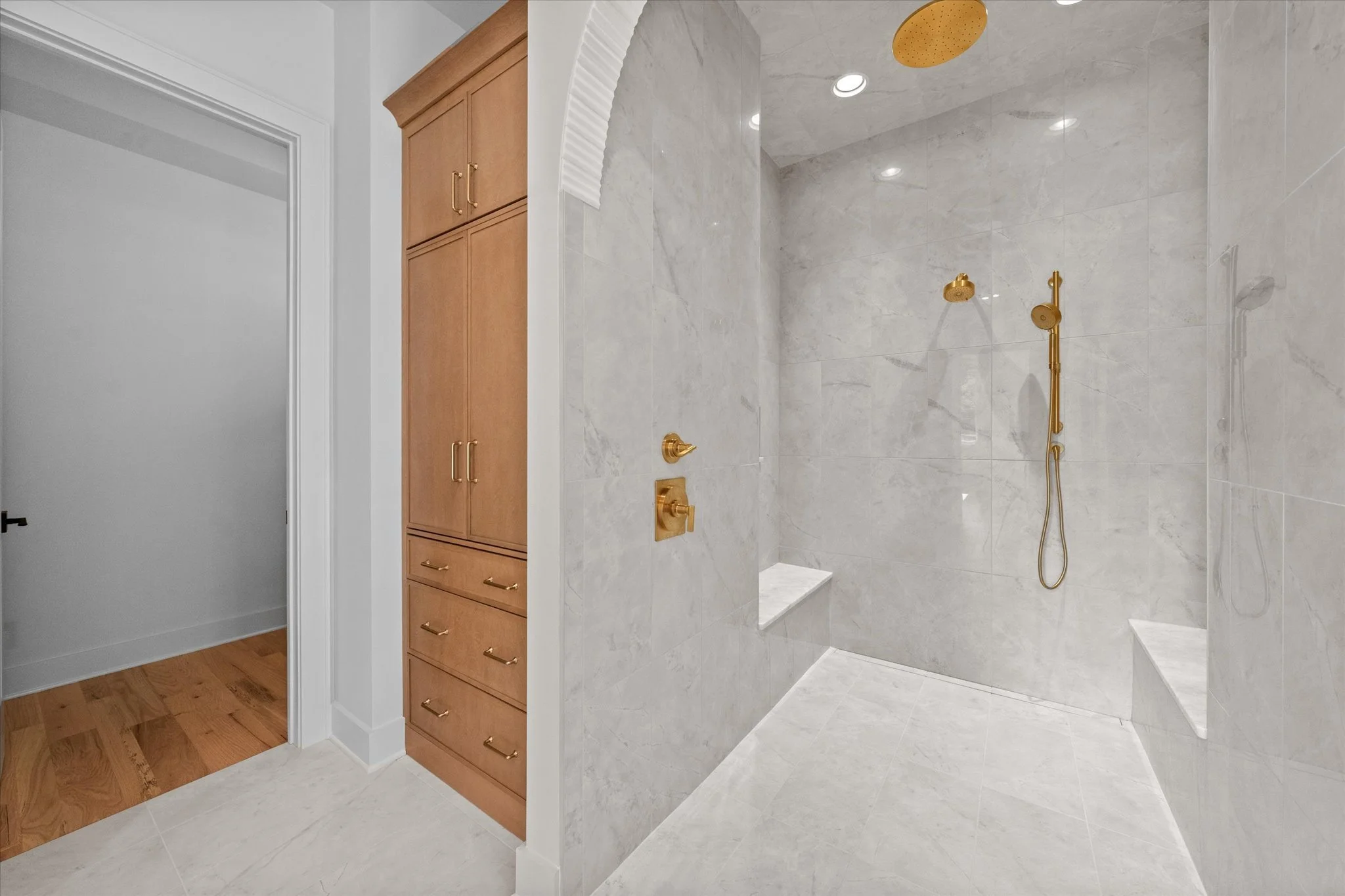 Modern walk-in shower with large marble tiles, gold fixtures, and built-in benches, with a dry section outside the shower.