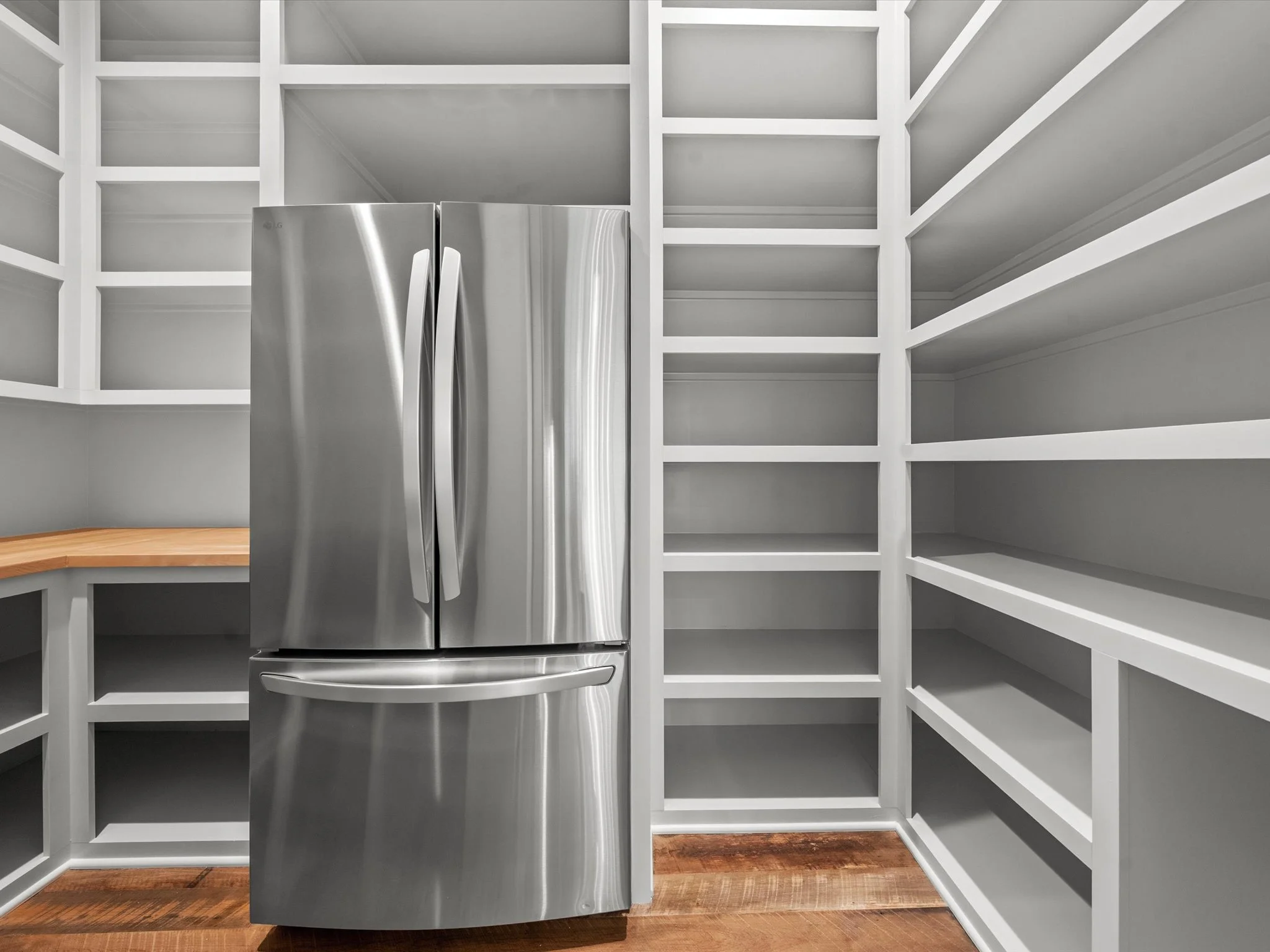 Empty kitchen pantry with built-in white shelves and a stainless steel refrigerator.