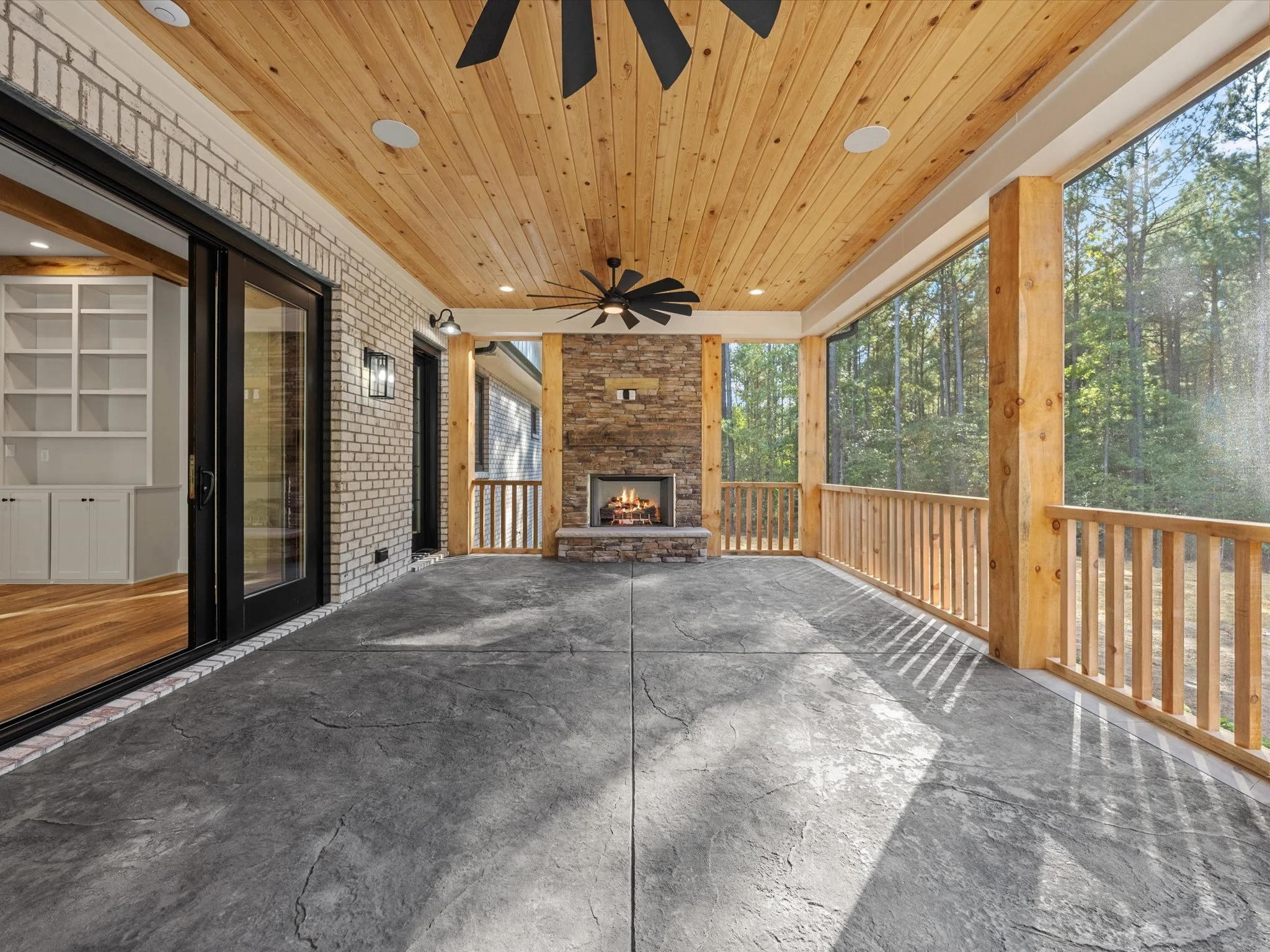 Covered porch with a stone fireplace, wooden ceiling, ceiling fan, and a view of trees outside