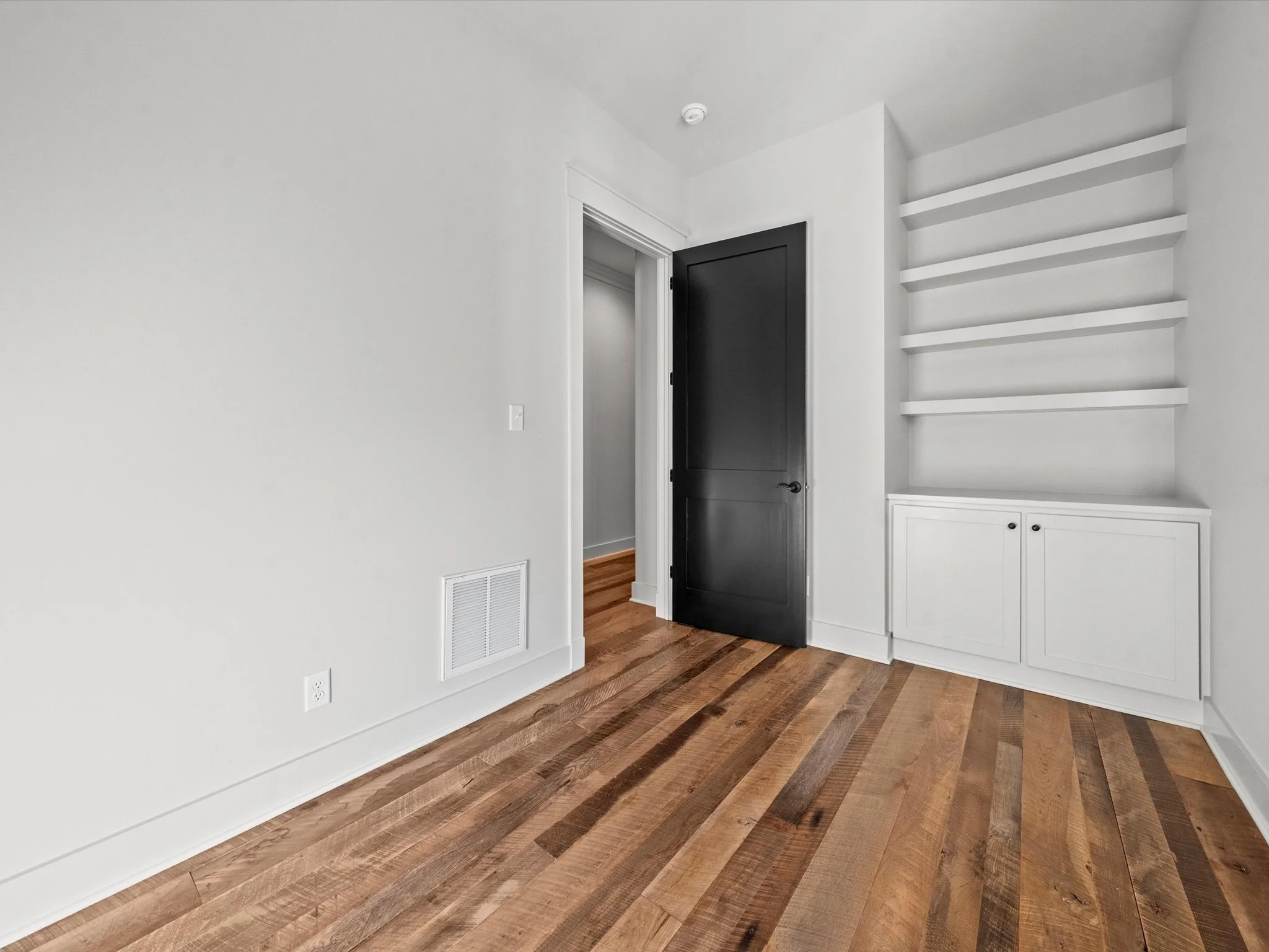 Empty room with white walls, hardwood floor, black door, built-in white shelving and cabinet.