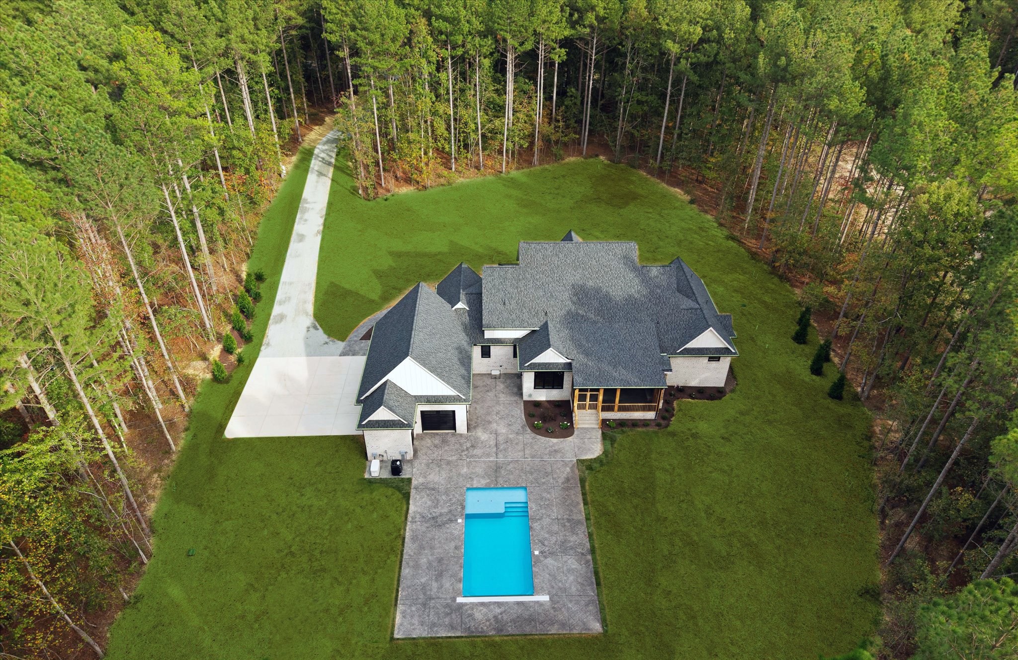 Aerial view of a modern house with a swimming pool, driveway, and spacious backyard surrounded by trees.