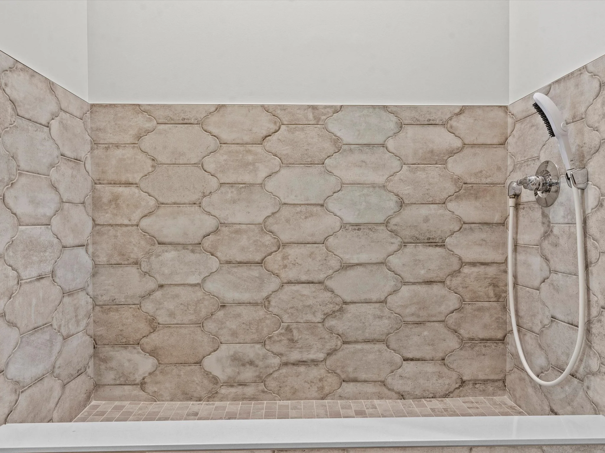 Empty shower with beige decorative tile walls and a handheld showerhead.