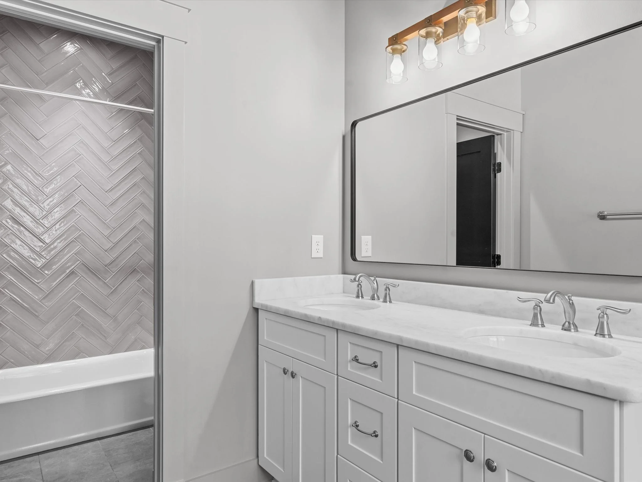 Bathroom with double sink vanity, large mirror, and a walk-in shower with gray herringbone tile.