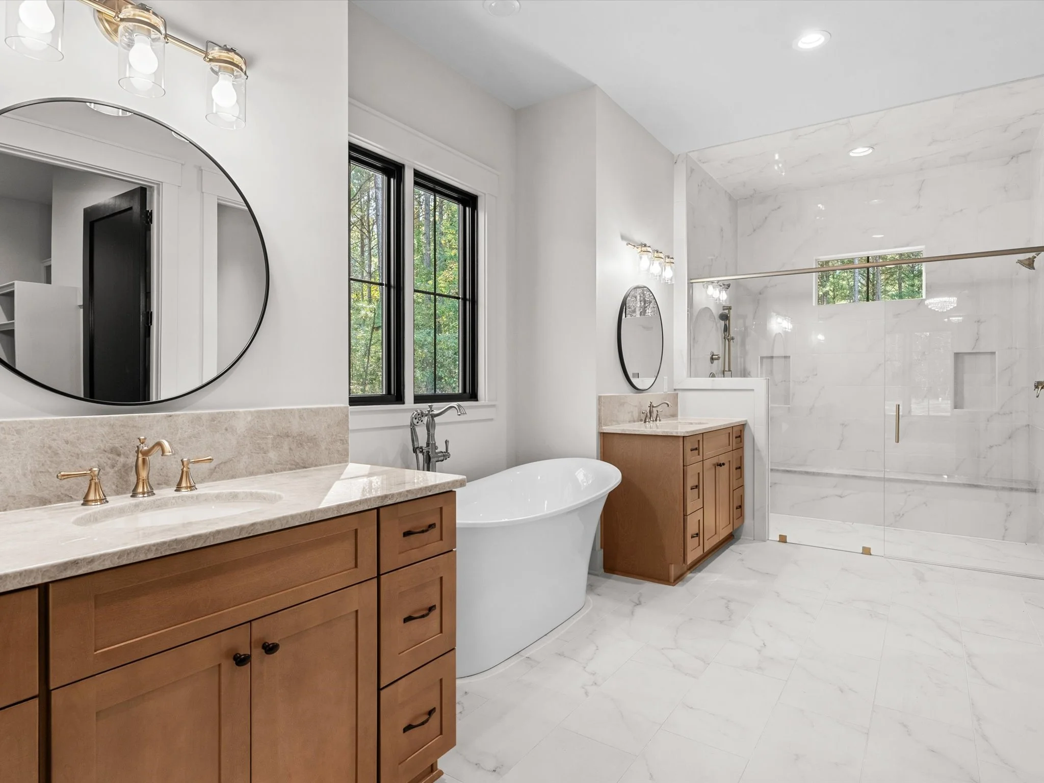 Modern bathroom with large marble shower, wooden vanities, a freestanding bathtub, and black-framed windows.