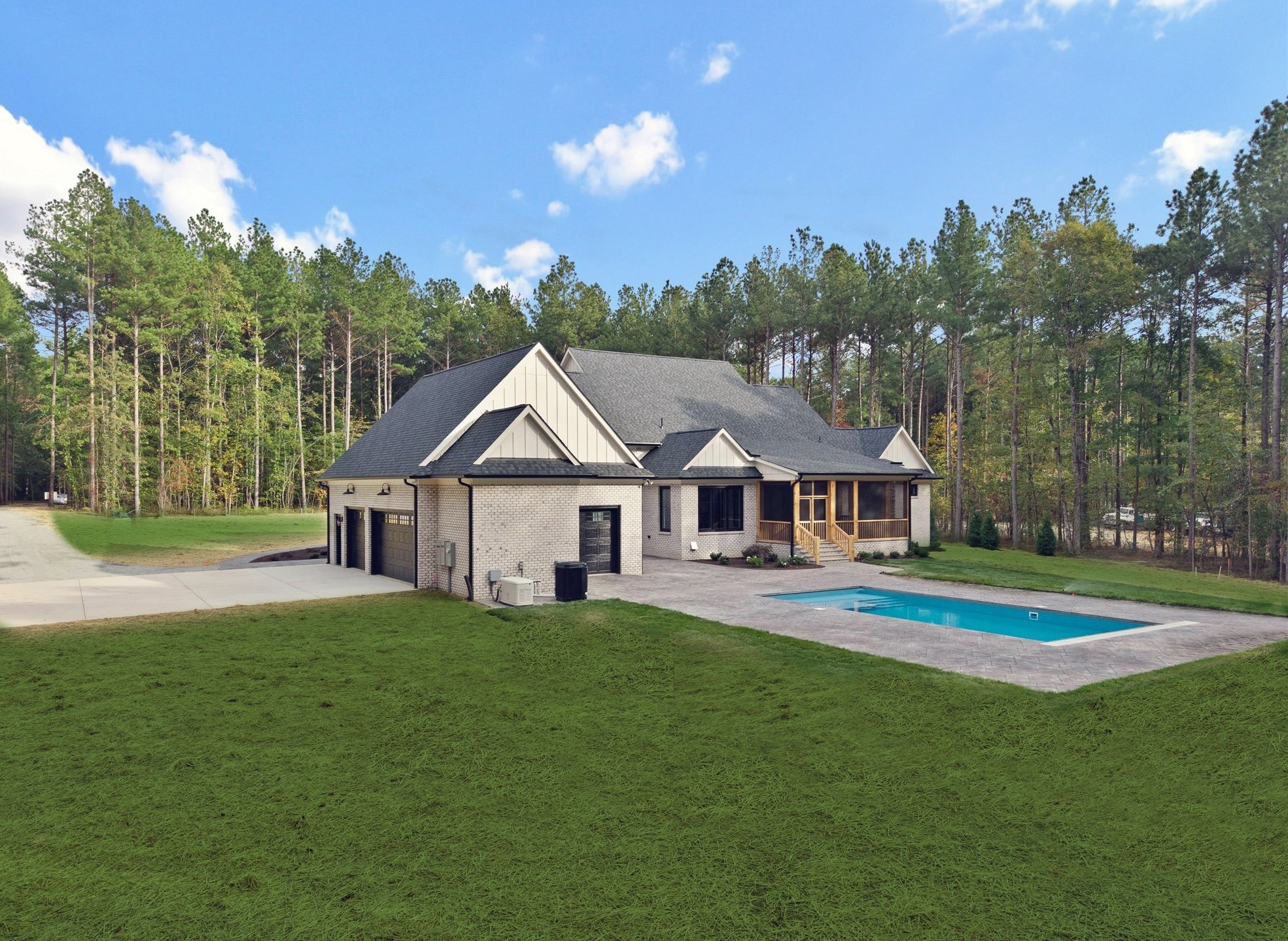 A modern house with a gray roof, white brick exterior, attached garage, a backyard with a swimming pool, surrounded by green grass and tall trees under a blue sky.