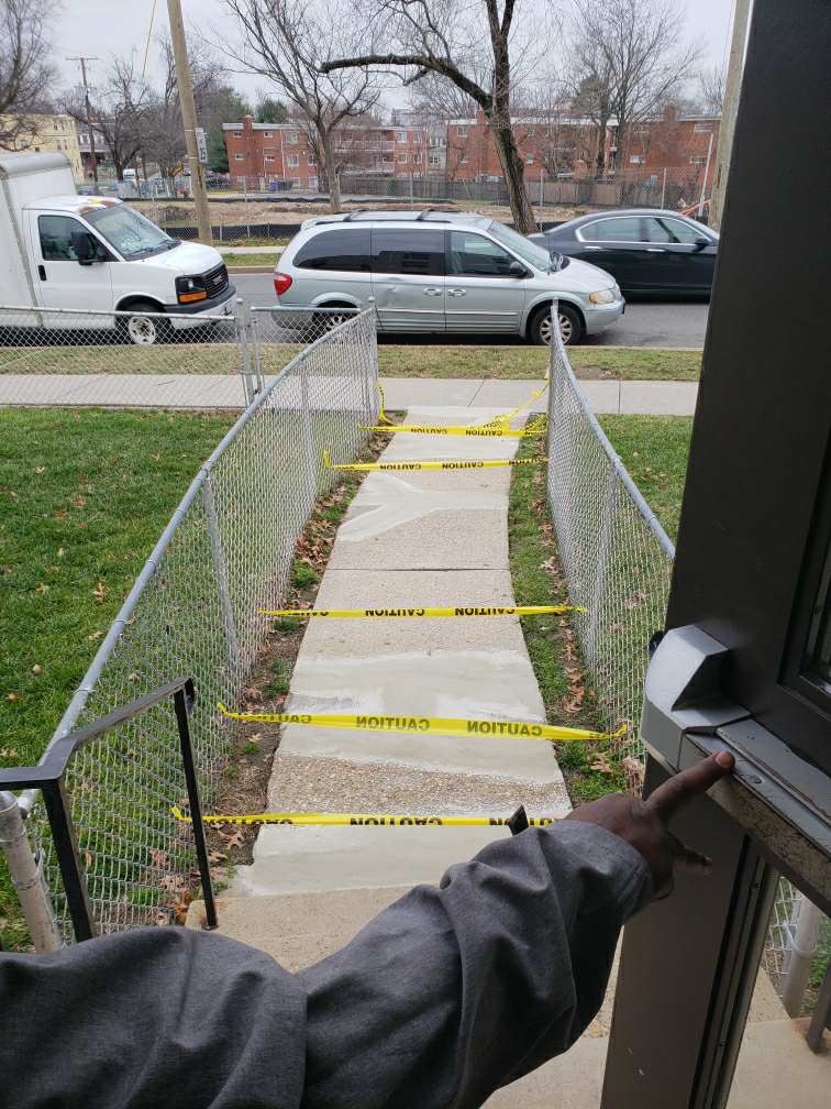 Photo taken after repairs were made to cracks in the sidewalk in front of a building on Saratoga Ave. at Brookland Manor. Because of Mid-City’s erected barbed wire fences, which block the community from grassy areas in their own neighborhood, residents were effectively locked in their homes until the concrete dried.