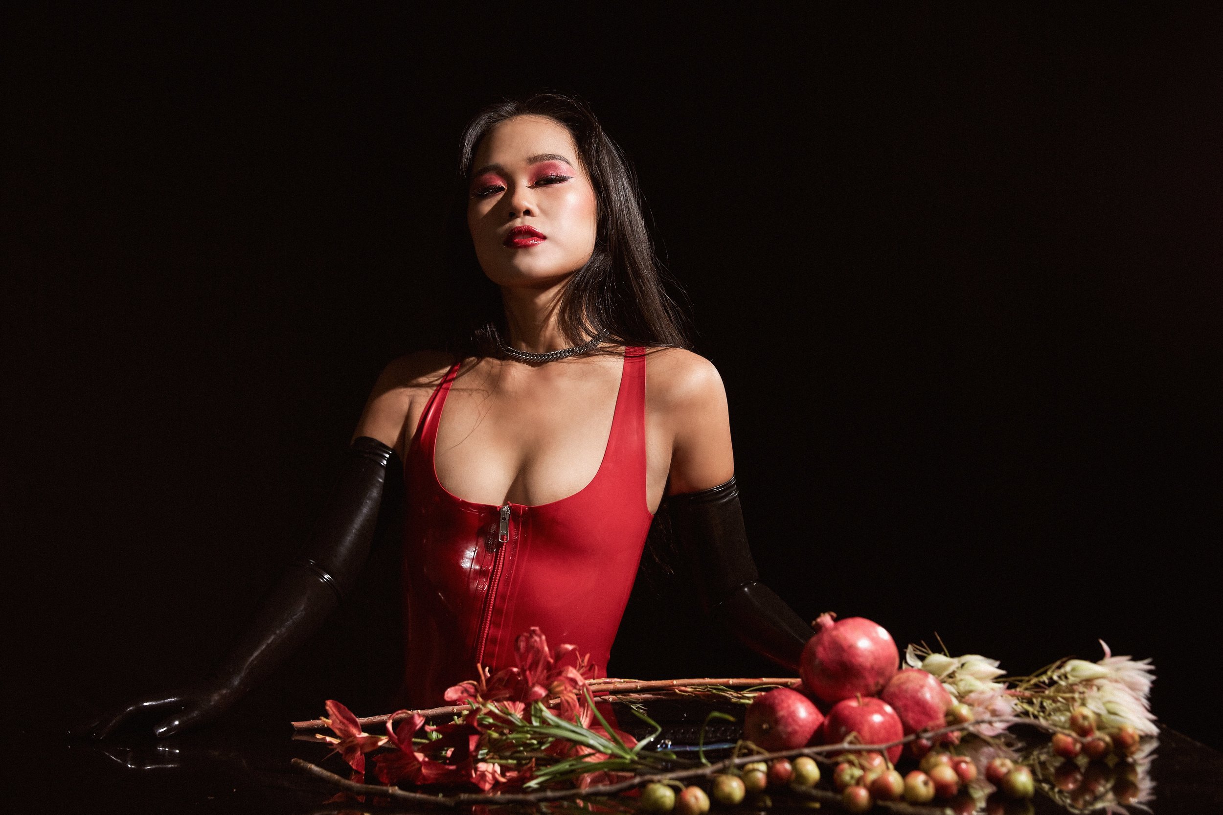 Asian female dominatrix Empress Wu in a red latex dress and black latex opera gloves surrounding by the spoils of luxury