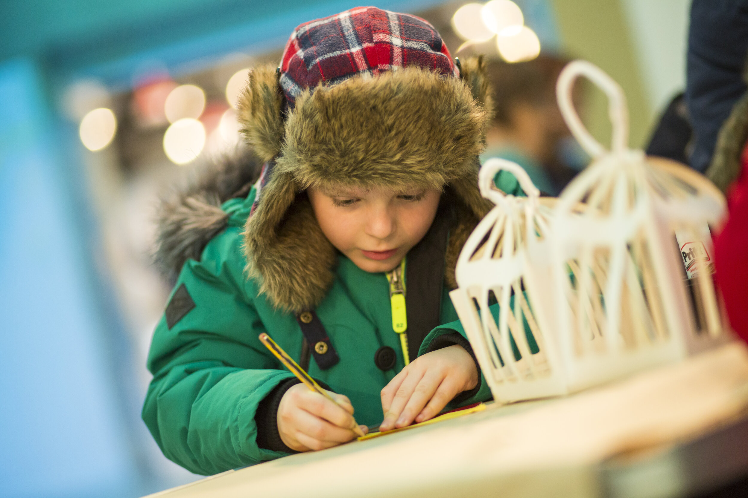  A child wearing a green coat writes with a pencil. 