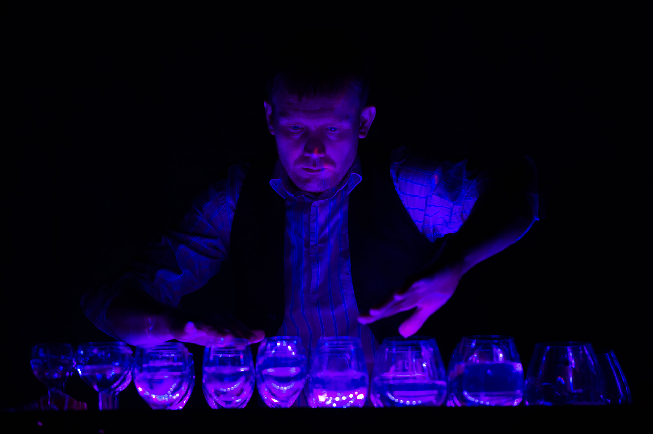  A blue and purple lit scene of water glasses being played. 