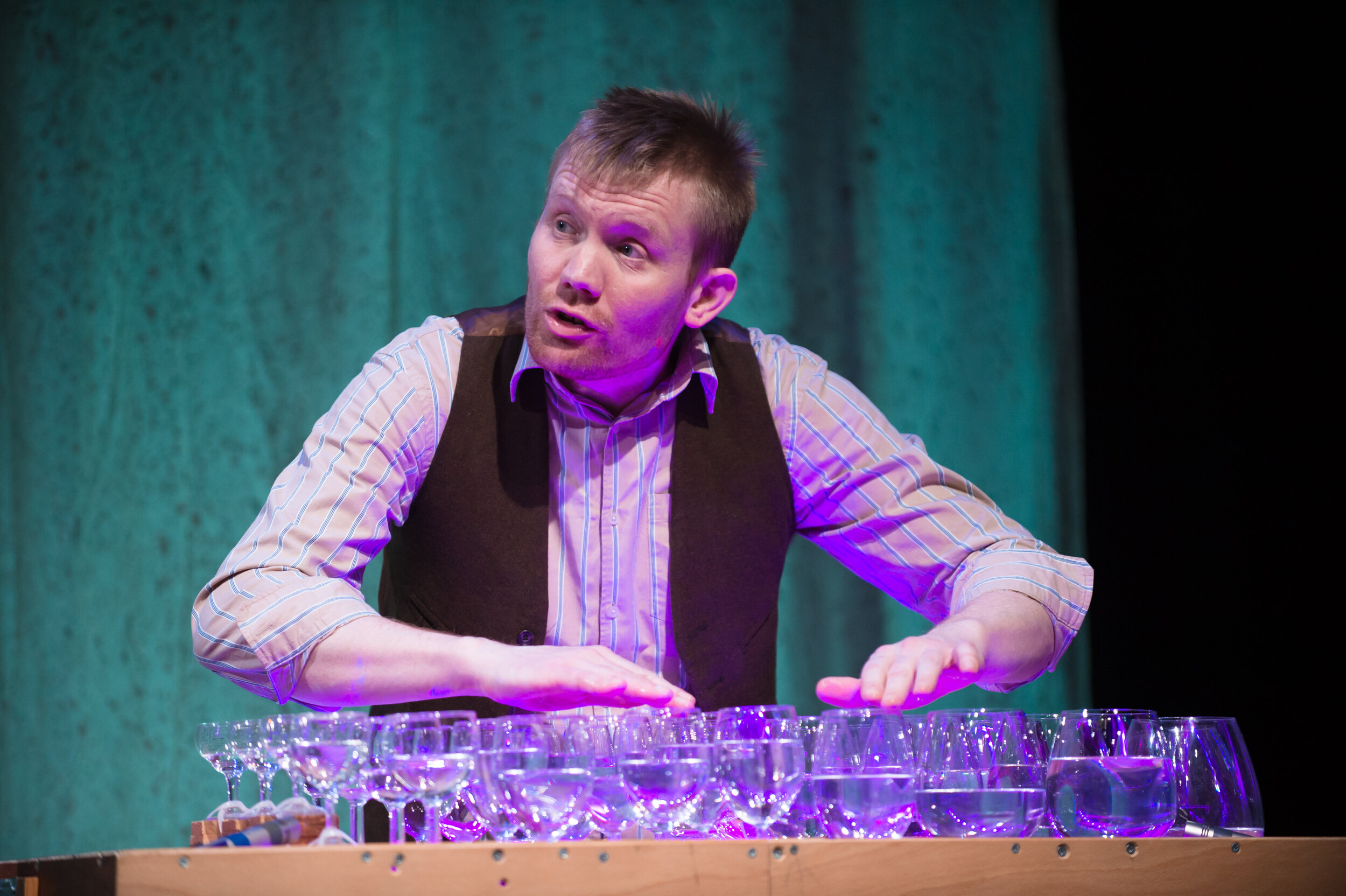  A table arranged with wine glasses filled with water, being played with fingers. 
