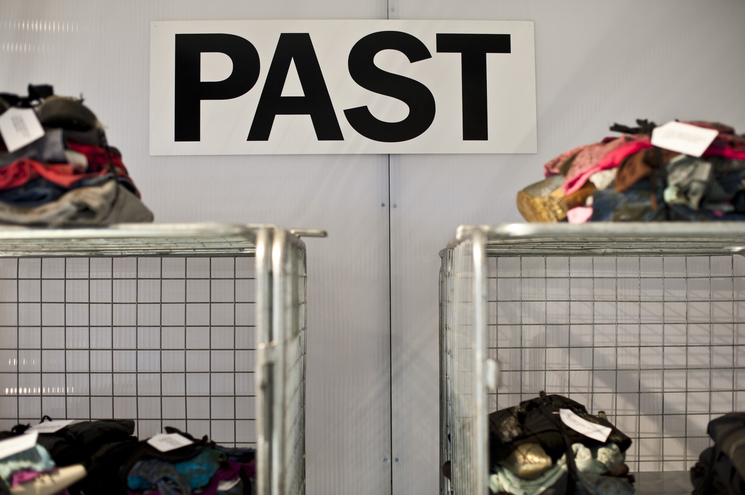  the word ‘past’ in large typeface is on the wall, objects sit on shelves below it. 