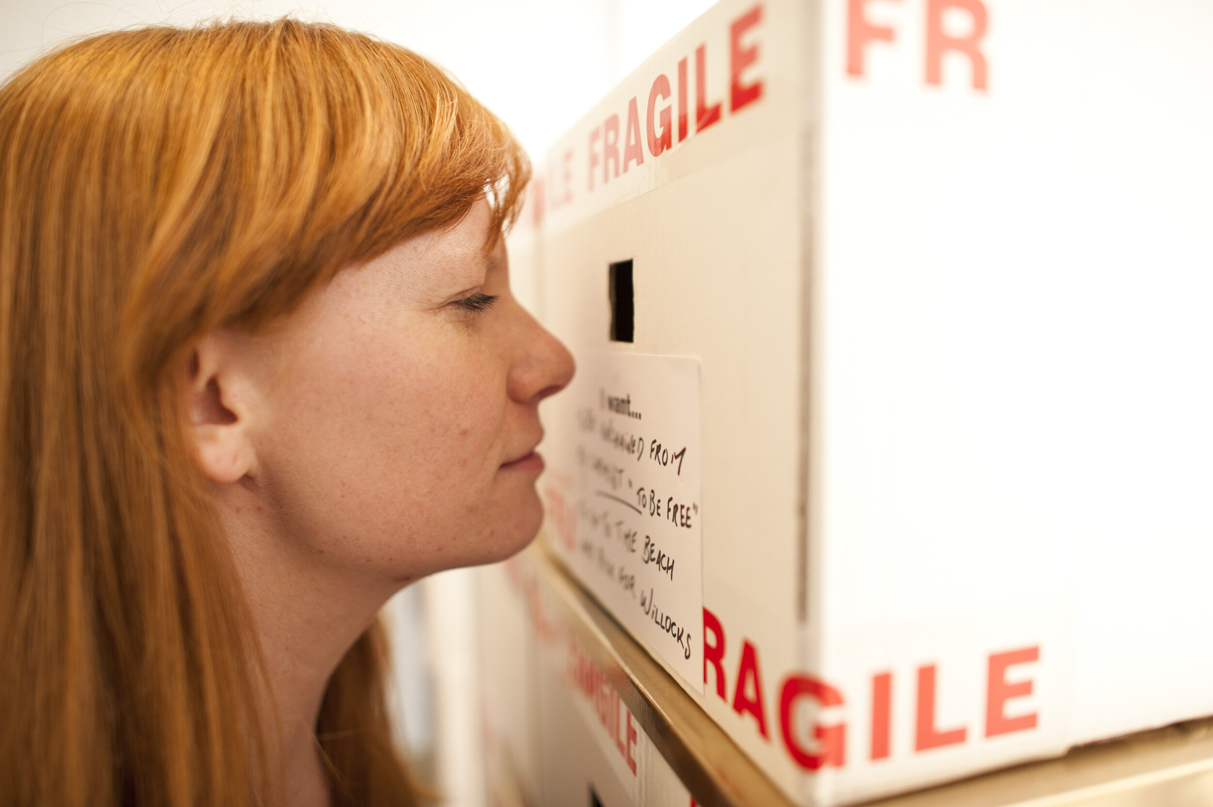  A woman peers into a cardboard box with fragile tape on it. 