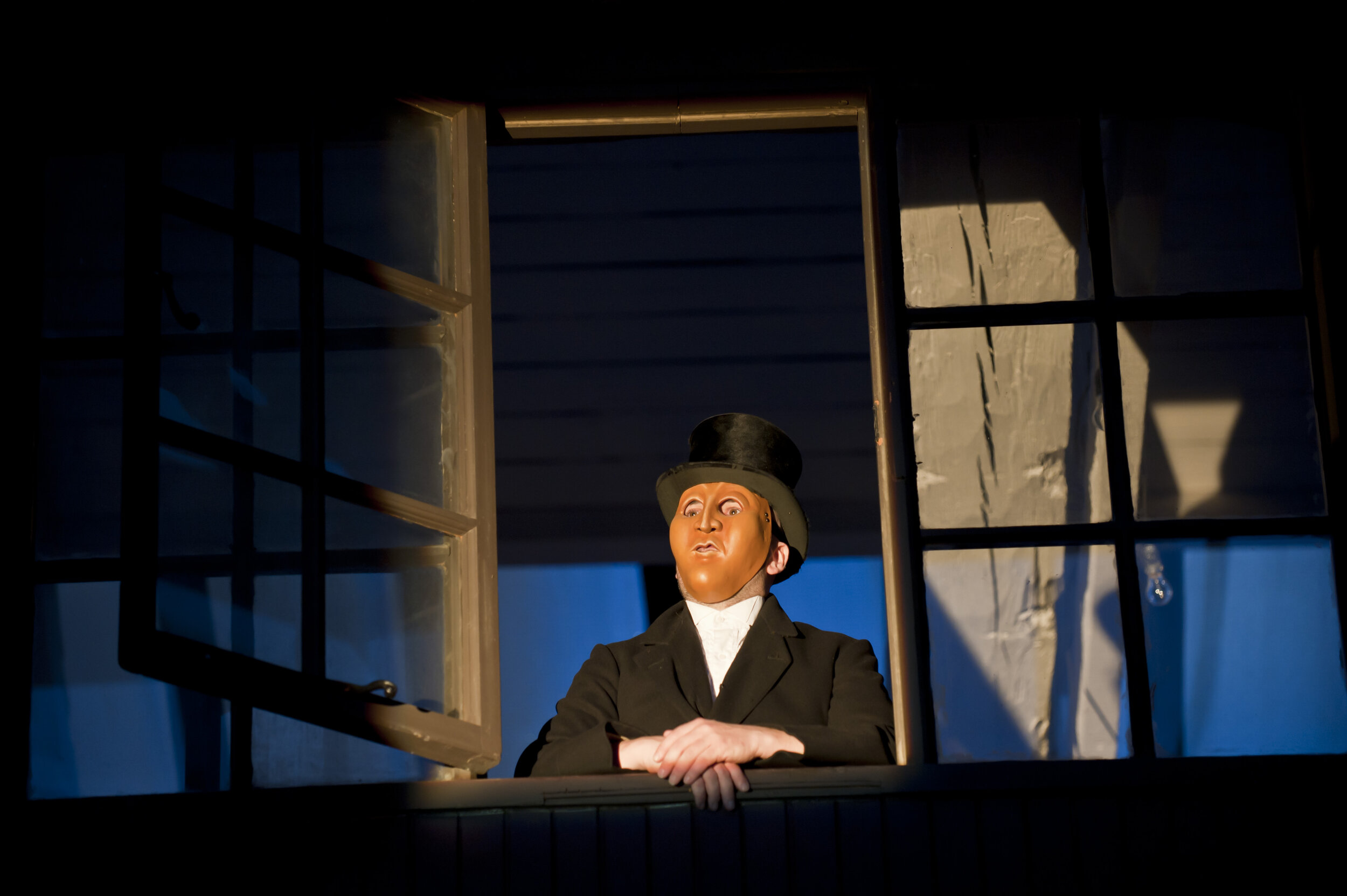  a man in a top hat and mask looks out of a window. 