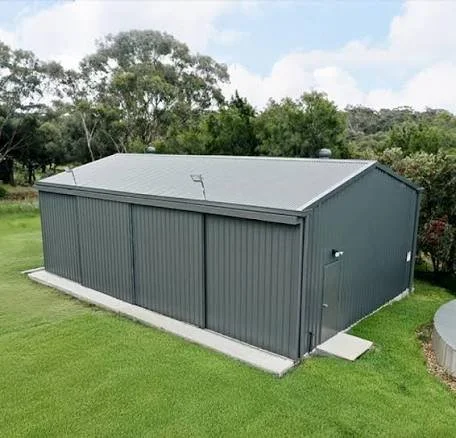 Gray metal storage shed on a concrete foundation with a small ramp leading to the door, surrounded by green grass and trees.