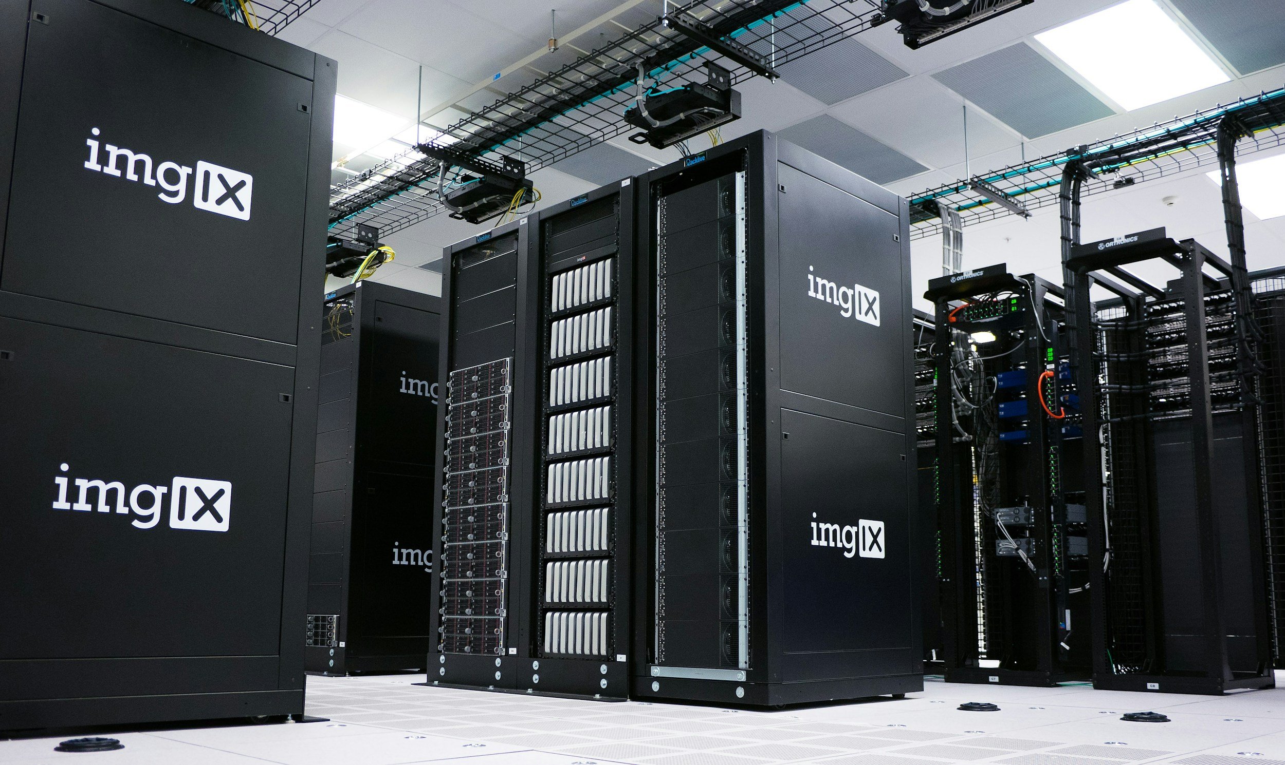 Data center with black server racks labeled 'imgLX' containing various electronic equipment and cables.