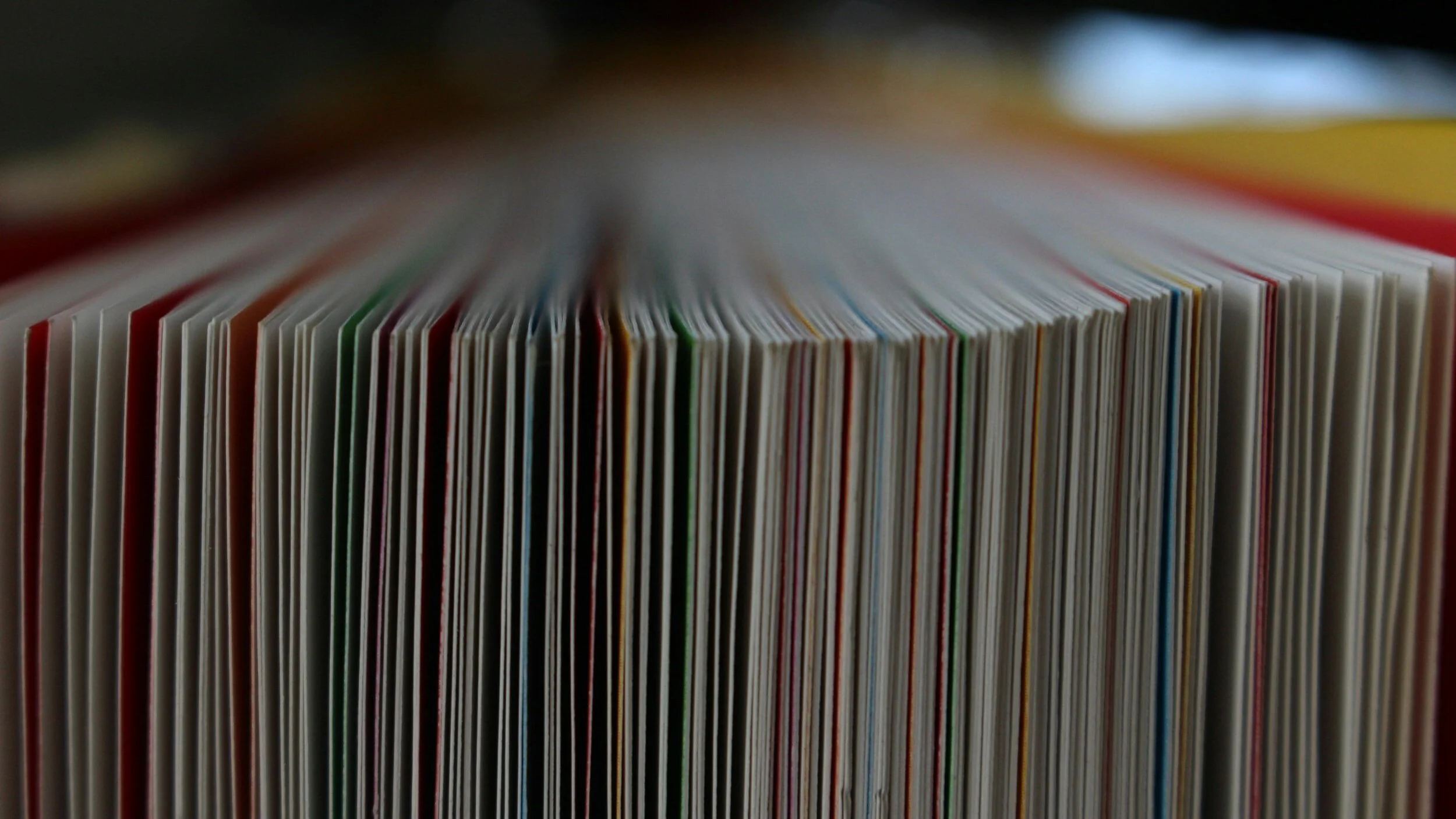 Close-up of a stack of colorful magazines or books, viewed from the side with the pages slightly fanned out.