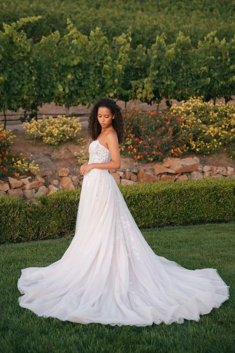  Shimmering sequin lace appliqués flow over layers of soft tulle in this romantic ballgown. A strapless, subtle cat-eye neckline highlights a corseted, exposed-boning bodice that defines the basque waist before opening into a full, airy skirt. Blendi