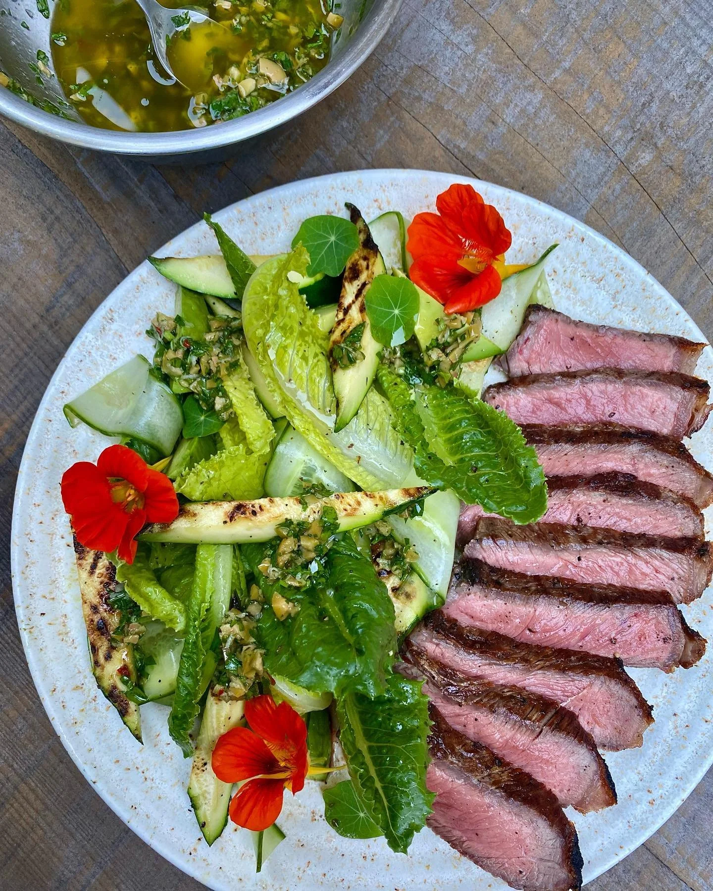 The salad that requires a grill. Every bite tastes the way summer smells and you&rsquo;ll dream about it for days. Grilled peppery steak and baby zucchini with shaved cucumber, avocado, crunchy lettuces, sweet nasturtium and green olive vinaigrette.